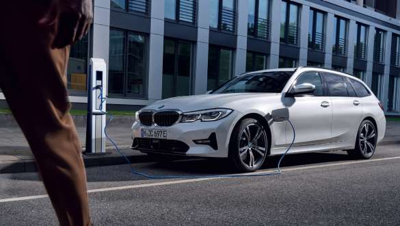 Plug-in hybrid BMW 3 Series Touring 2021 G21 three-quarter front view charging Plug-in hybrid BMW 3 Series Touring 2021 G21 three-quarter front view charging in front of a building