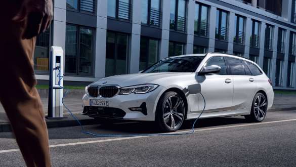 Plug-in hybrid BMW 3 Series Touring 2021 G21 three-quarter front view charging Plug-in hybrid BMW 3 Series Touring 2021 G21 three-quarter front view charging in front of a building