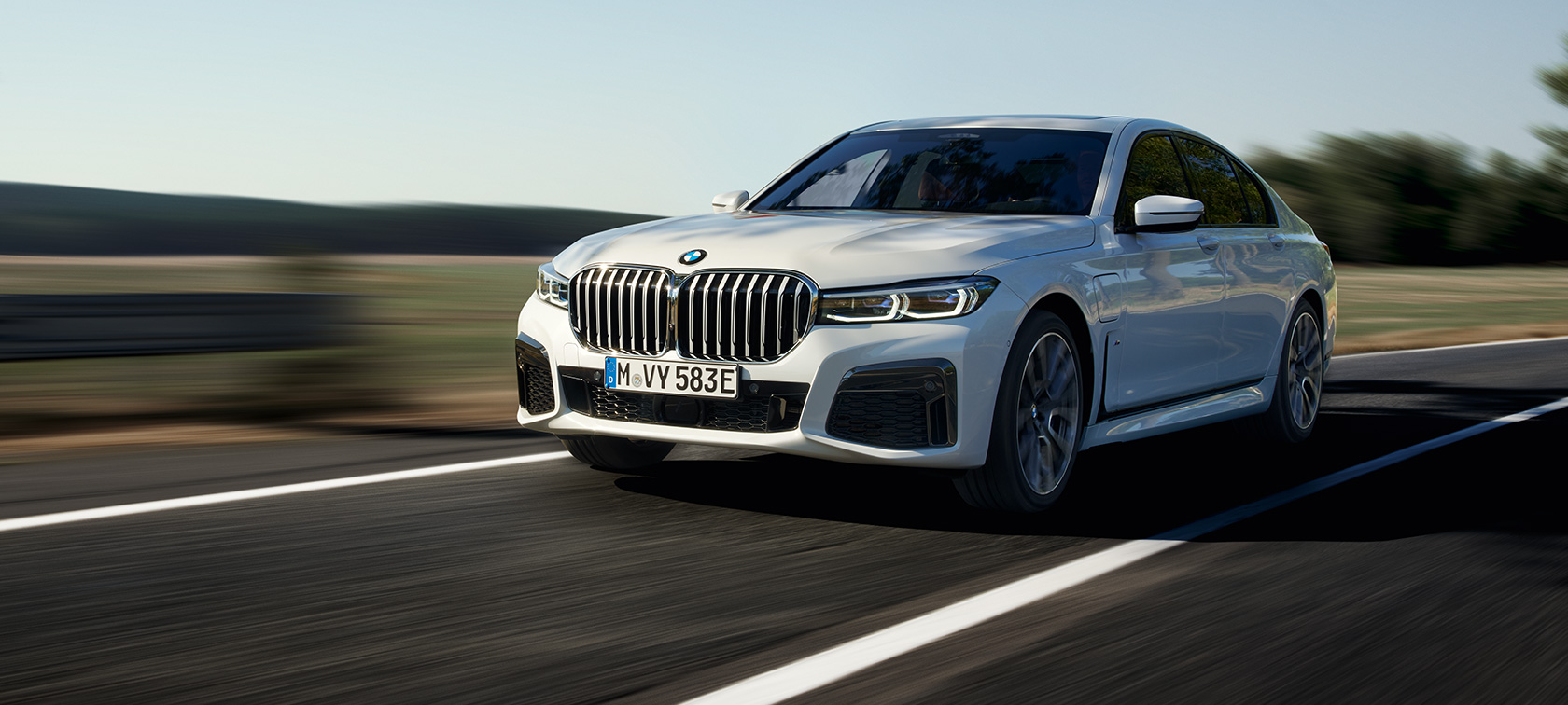 BMW 745e Sedan plug-in hybrid G11 G12 Mineral White three-quarter front view BMW 745e Sedan plug-in hybrid G11 G12 Mineral White metallic three-quarter front view driving on country road