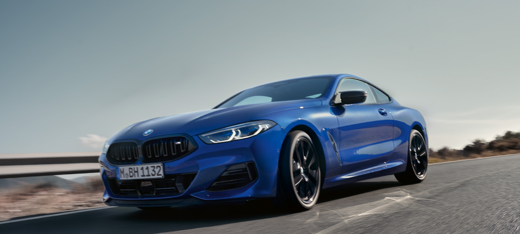 BMW 8 Series Coupé G15 LCI Facelift 2022 BMW M850i xDrive M Portimao blue metallic front view low-angle shot BMW 8 Series Coupé G15 LCI Facelift 2022 BMW M850i xDrive M Portimao blue metallic front view low-angle shot driving on country road in with hills in the background