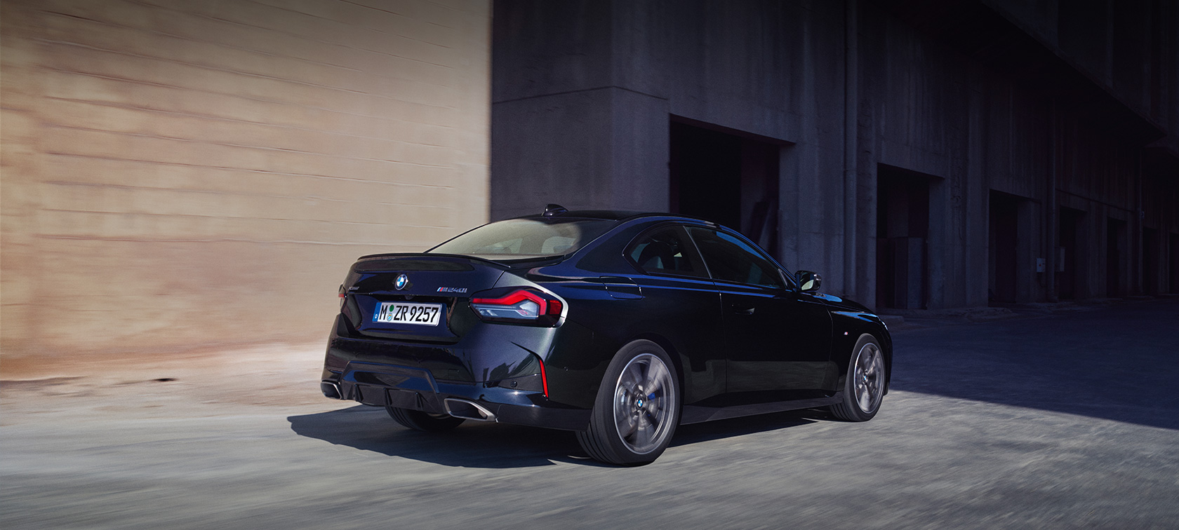 BMW M240i xDrive Coupé G42 2021 three-quarter rear view driving BMW M240i xDrive Coupé G42 2021 Black Sapphire metallic three-quarter rear view driving