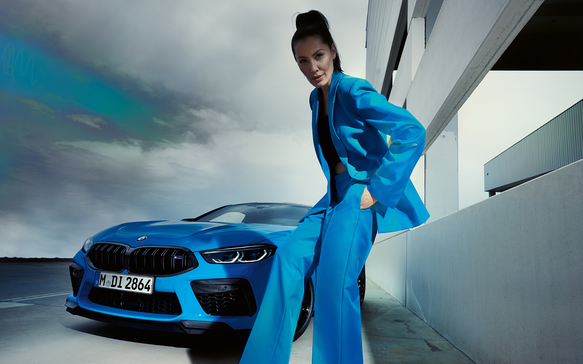 The BMW M8 Competition Coupé F92 LCI 2022 three-quarter front view The BMW M8 Competition Coupé F92 LCI Facelift 2022 Daytona Beach blue uni three-quarter front view with a female model in blue trouser suit