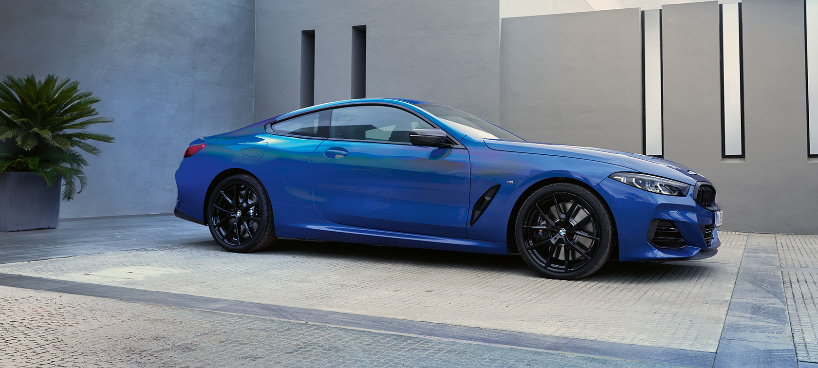 Side view the BMW M850i xDrive Coupé G15 LCI Facelift 2022 The BMW M850i xDrive Coupé G15 LCI Facelift 2022 M Portimao Blue metallic side view standing in front of a building