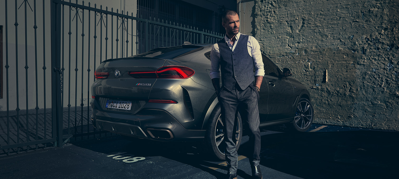 BMW X6 M50i in three-quarter rear view G06 Man standing next to BMW X6 M50i G06 2018 SUV in three-quarter rear view
