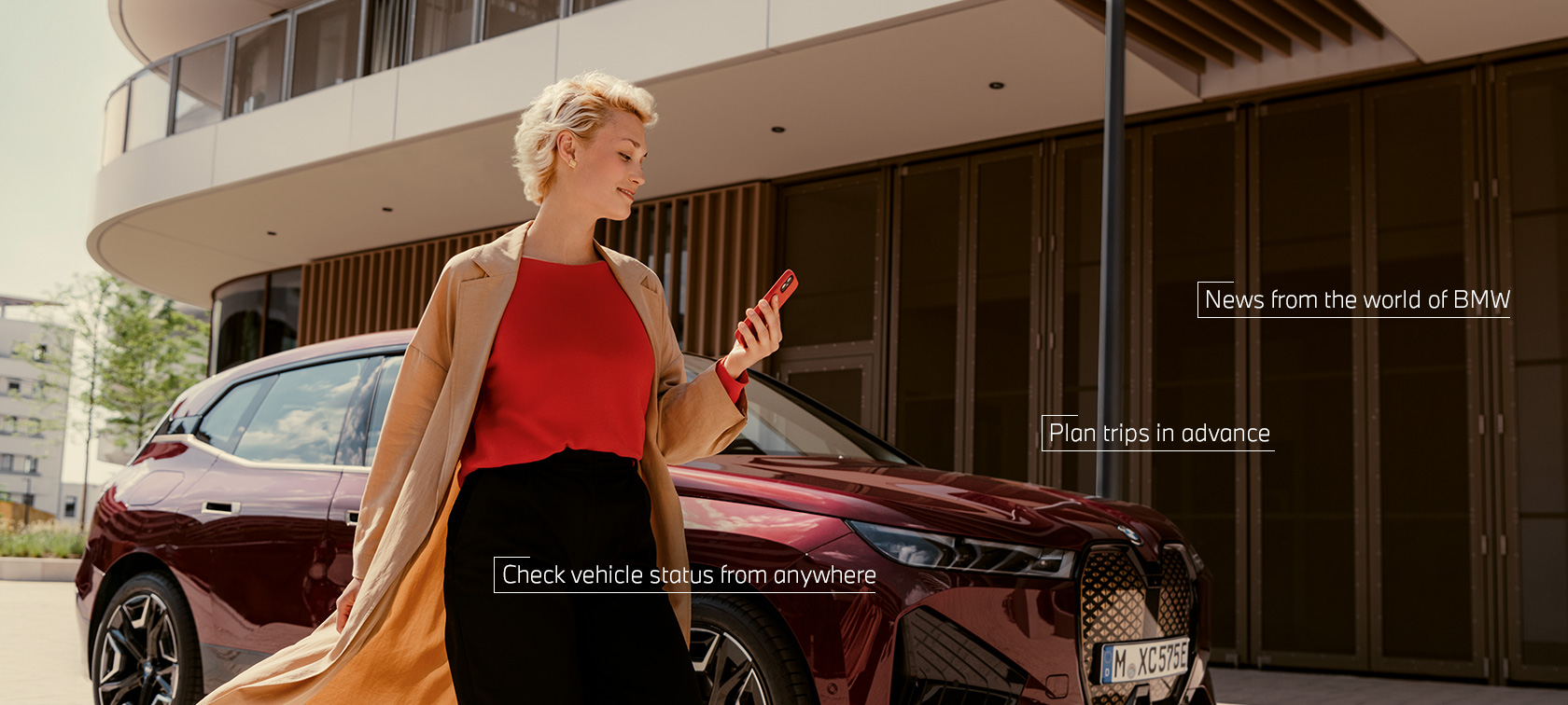 Woman in front of BMW iX uses My BMW app on smartphone Woman in front of BMW iX uses My BMW app on smartphone