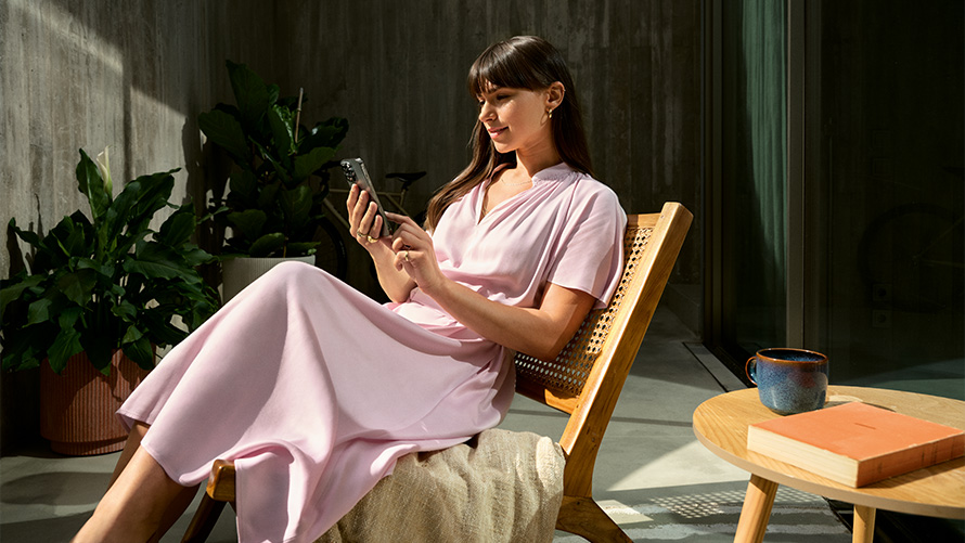 Woman in pink dress holding smartphone Remote Inside View Remote Inside View Woman in pink dress with smartphone in hand on a chair