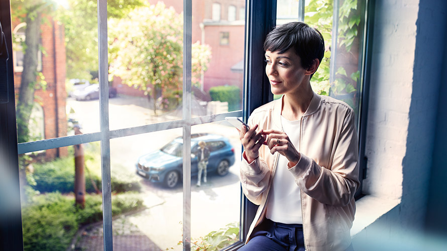 Share Live Trip Status Woman sits in front of window and uses Share Live Trip Status on smartphone