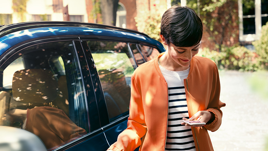 BMW offers summer BMW Teleservices BMW offers summer BMW Teleservices woman stands in front of BMW and uses smartphone