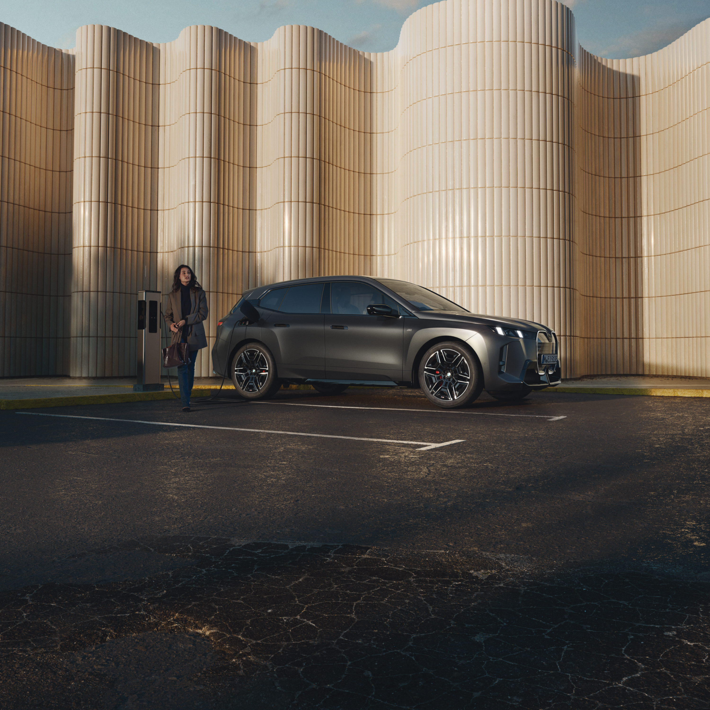 Person leaning against a BMW at a public charging post at the side of the road