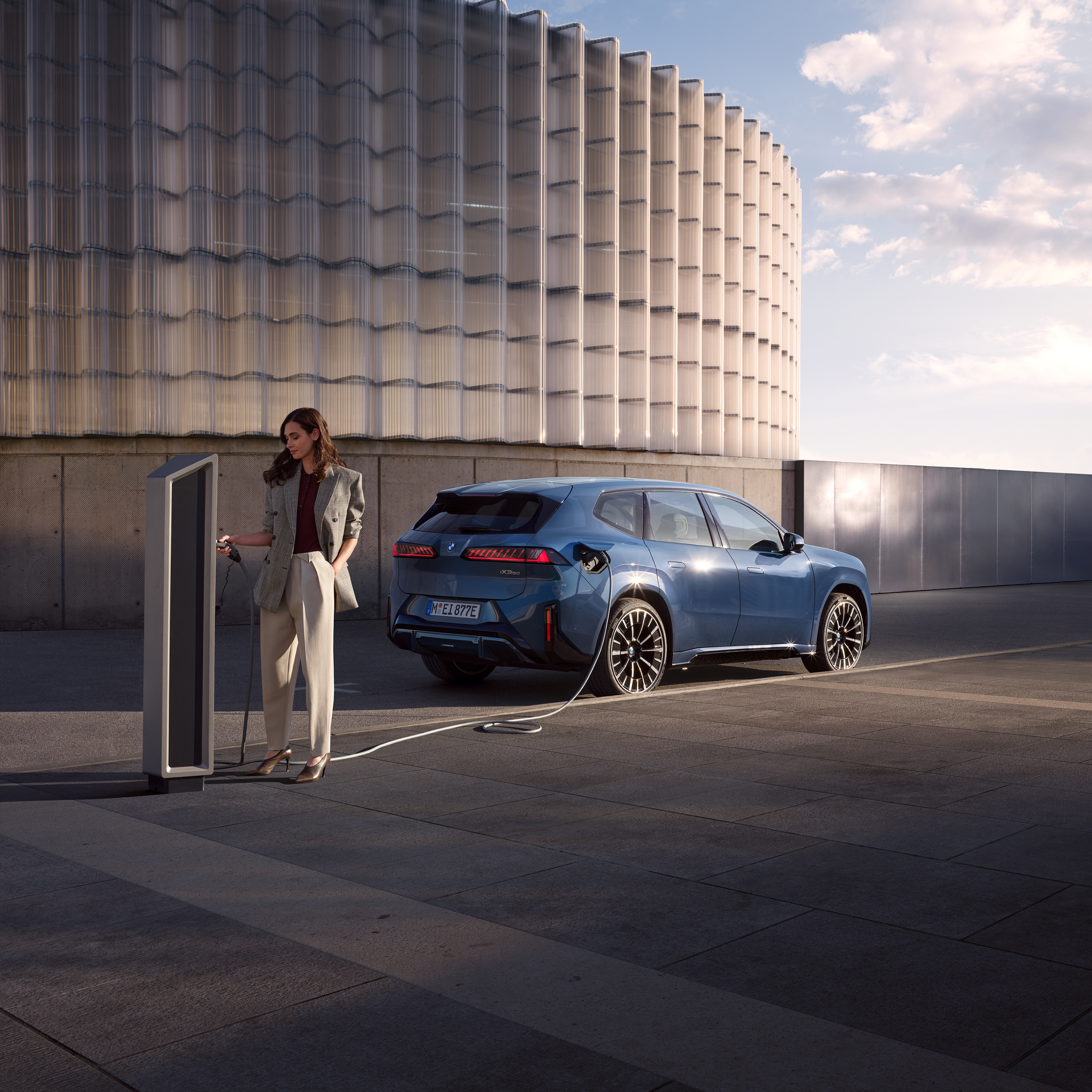 A woman is standing next to a BMW iX3, which is connected to a public charging station