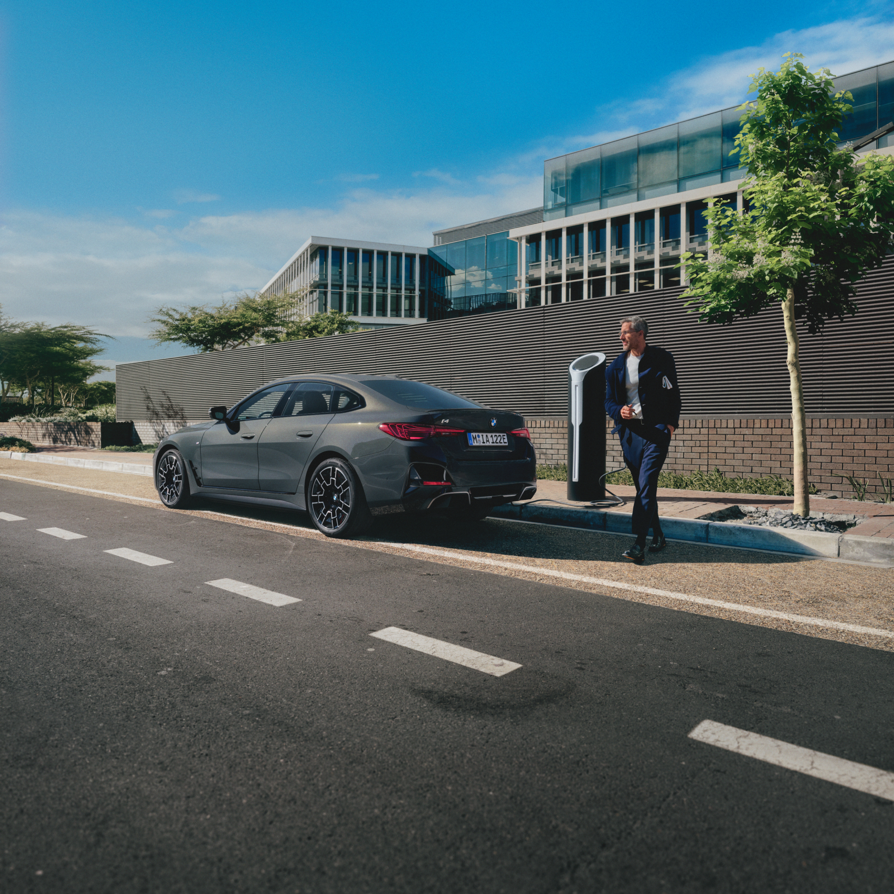 Person standing behind a charging BMW at the side of the road